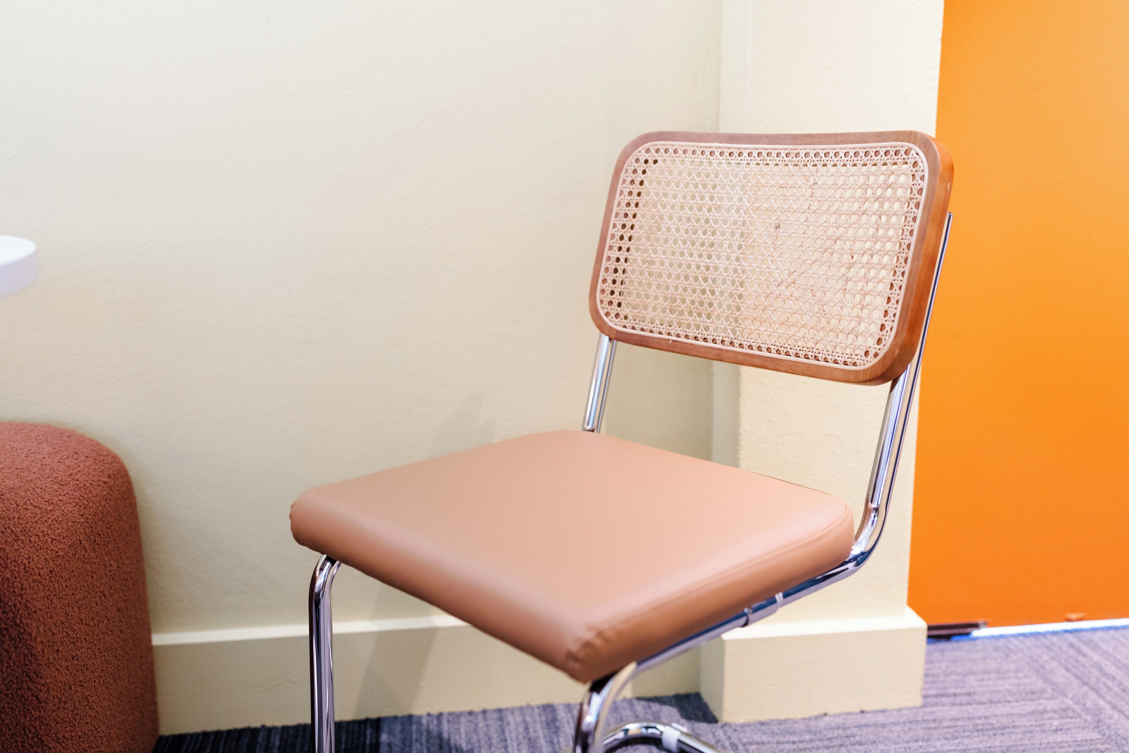 Une chaise dotée d’un dossier en osier et d’un siège rembourré, placée contre un mur aux couleurs blanc et orange.