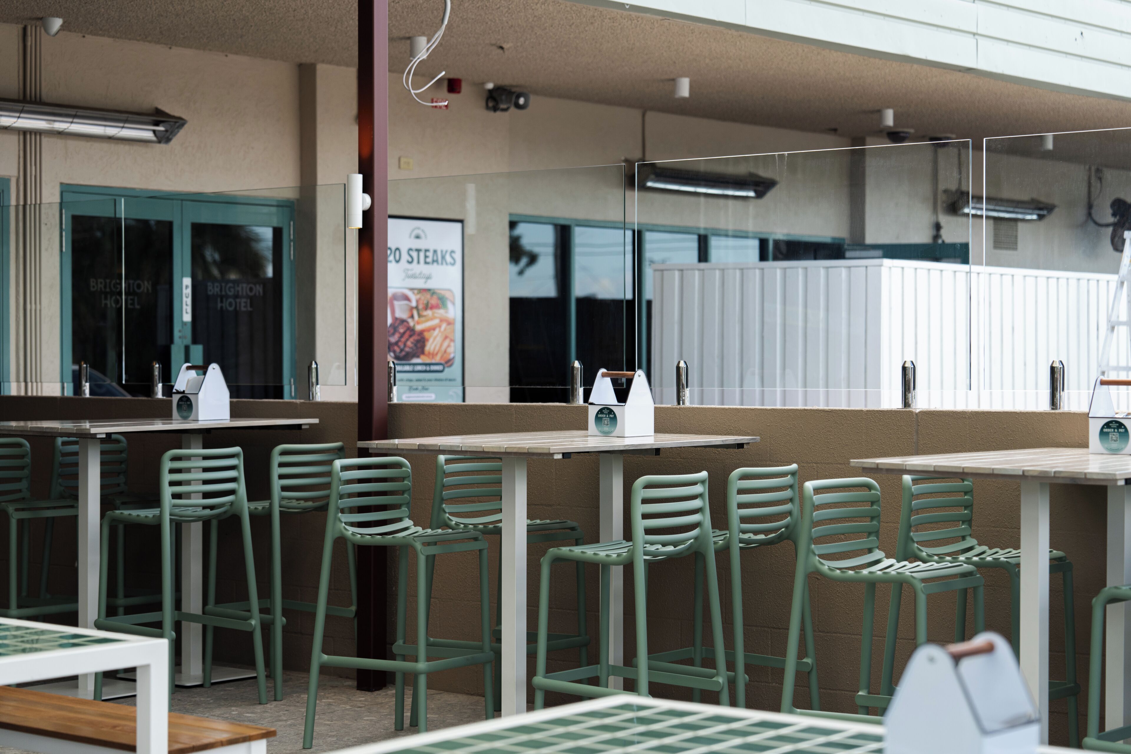 A restaurant with outdoor seating, including green chairs and tables, and a sign advertising steaks.