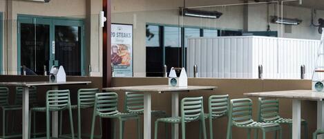 A restaurant with outdoor seating, including green chairs and tables, and a sign advertising steaks.