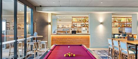 Une table de billard dans une pièce bien éclairée, avec un bar et des sièges.