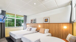 Una habitación de hotel con dos camas, una mesita redonda y un televisor montado en la pared.