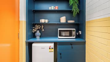 Una piccola cucina compatta con forno a microonde, un frigorifero e scaffali con stoviglie.