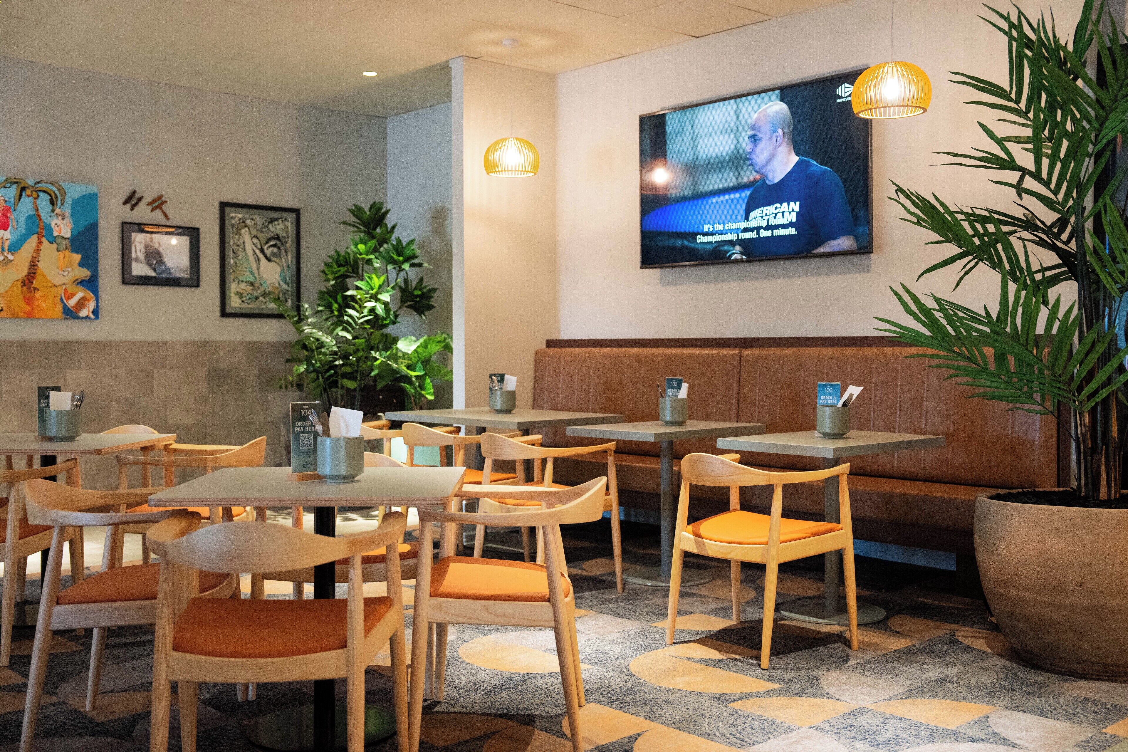 Un restaurante con mesas y sillas de madera, una pantalla de televisión grande y obras de arte enmarcadas en la pared.