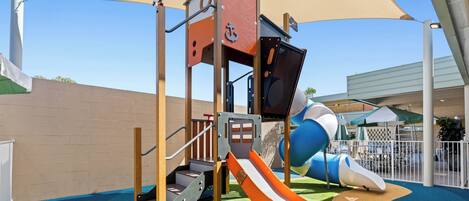 A playground with a slide, climbing structures, and a shaded area.