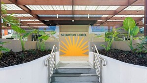 Una escalera conduce a la entrada del Hotel Brighton, rodeado de vegetación y un cielo despejado.