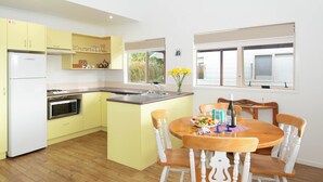 Una cocina con armarios amarillos, una mesa de comedor de madera con sillas blancas, un refrigerador y un microondas.