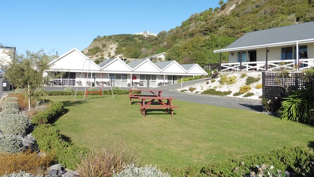 A row of white buildings with pitched roofs, a picnic table in the foreground, and a hill with trees in the background. - The Peninsula Kaikoura (Kaikoura)
