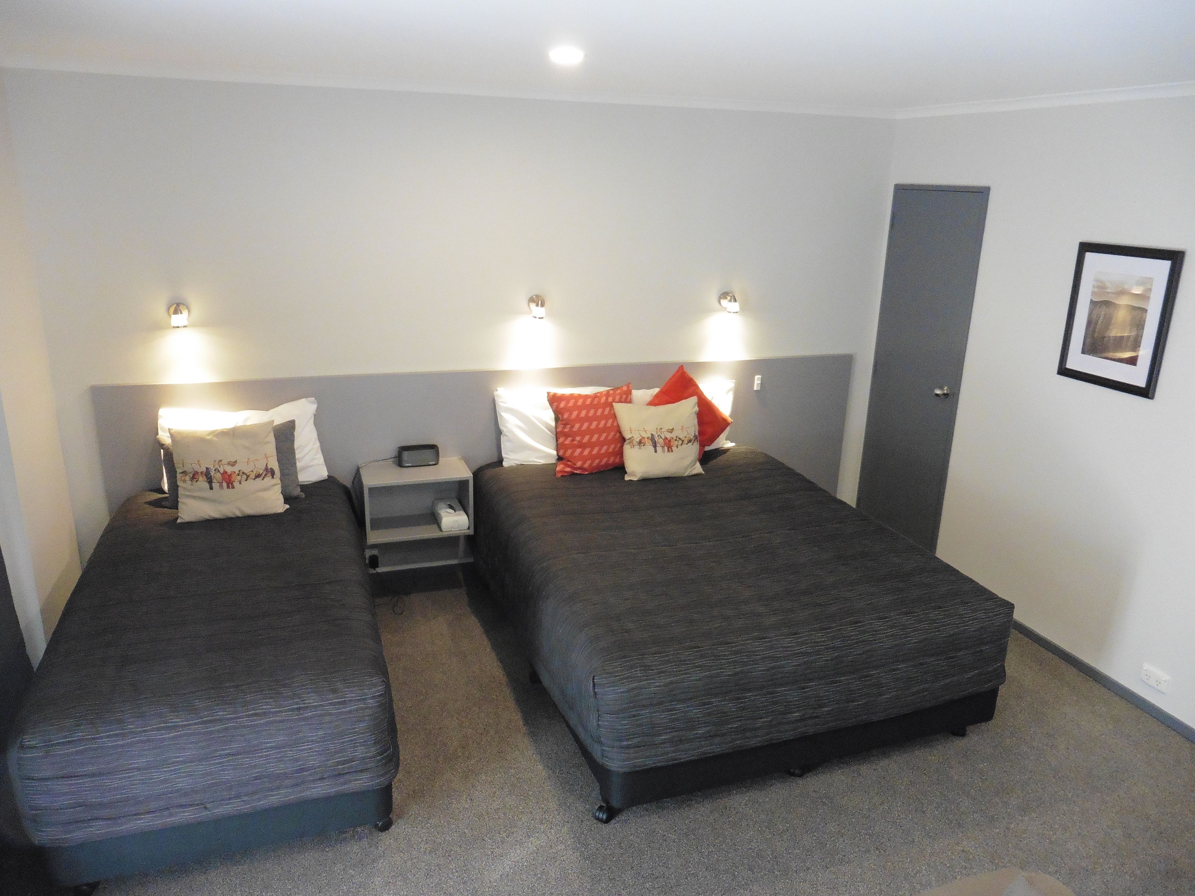 A hotel room with two single beds, each with a pillow and a bedside table with a lamp.