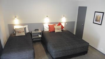 A hotel room with two single beds, each with a pillow and a bedside table with a lamp.