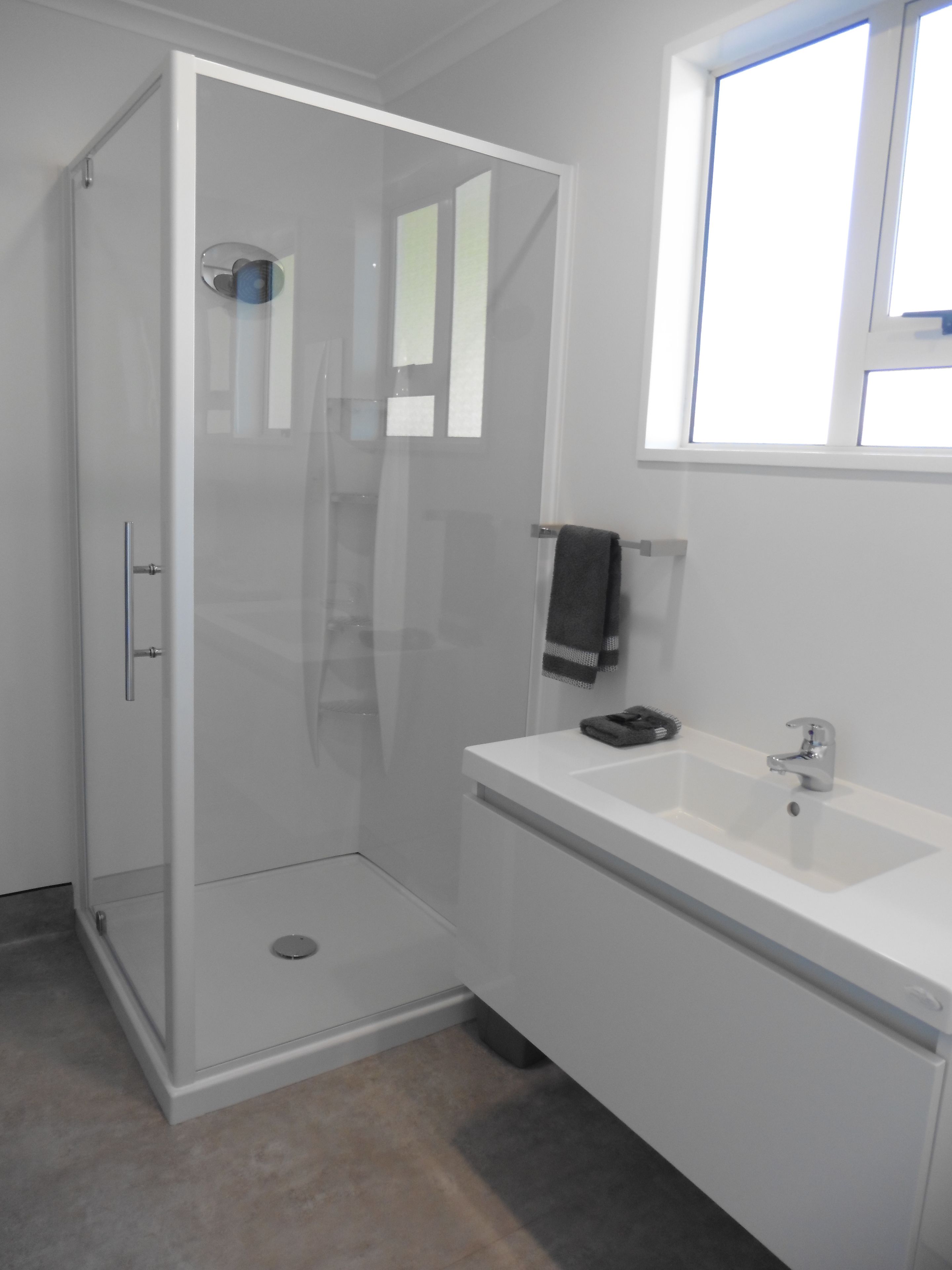 Un baño moderno con ducha de vidrio, un lavamanos blanco y una ventana sobre el lavamanos.
