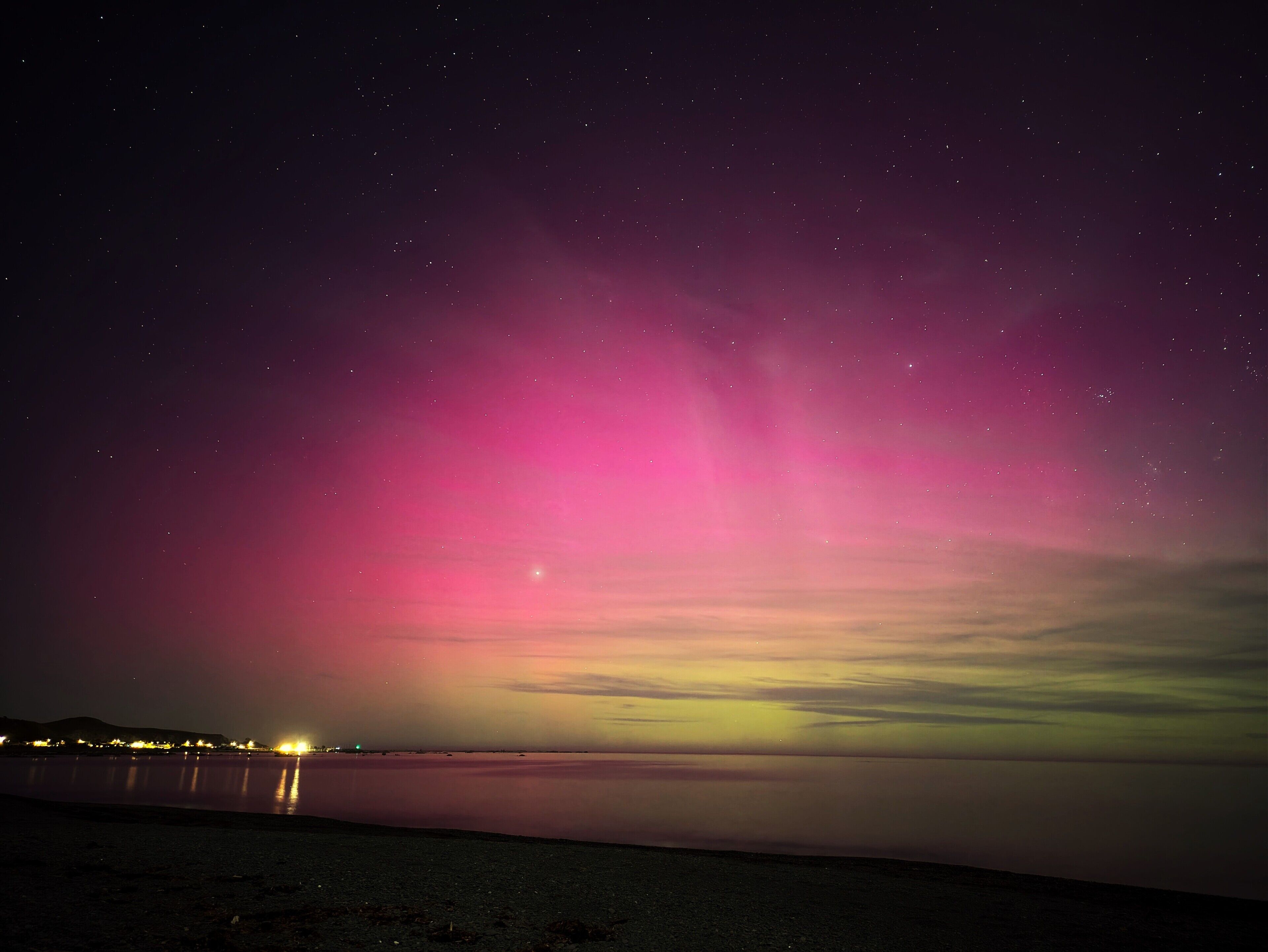 Un ciel nocturne étoilé et une aurore rose au-dessus d’une étendue d’eau calme.