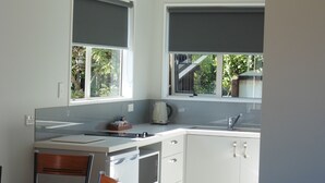 A modern kitchen with white cabinets, a built-in oven, and a dining area with a round table and chairs. - The Peninsula Kaikoura (Kaikoura)