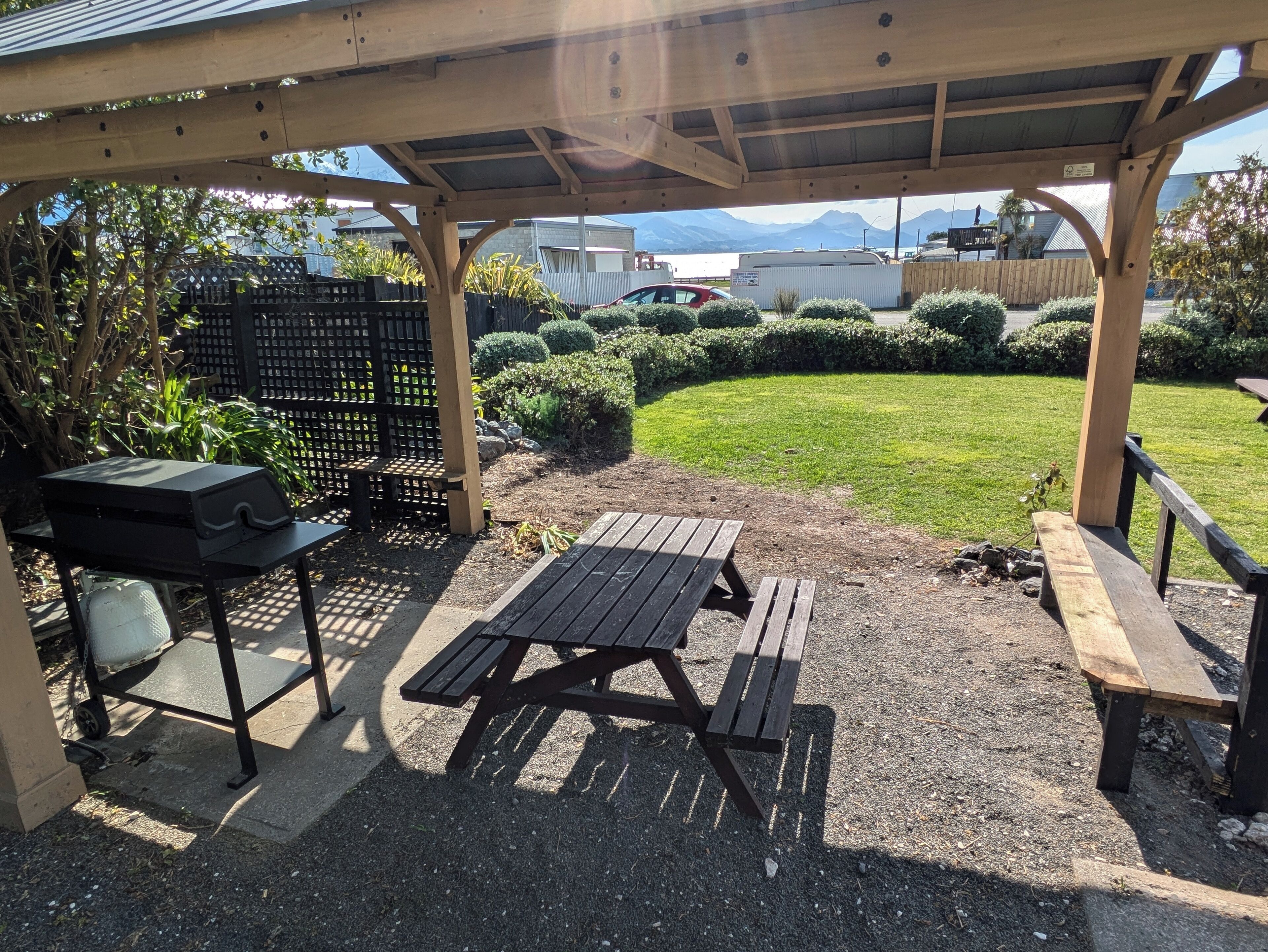 A covered outdoor area with a barbecue grill, picnic table, and benches.
