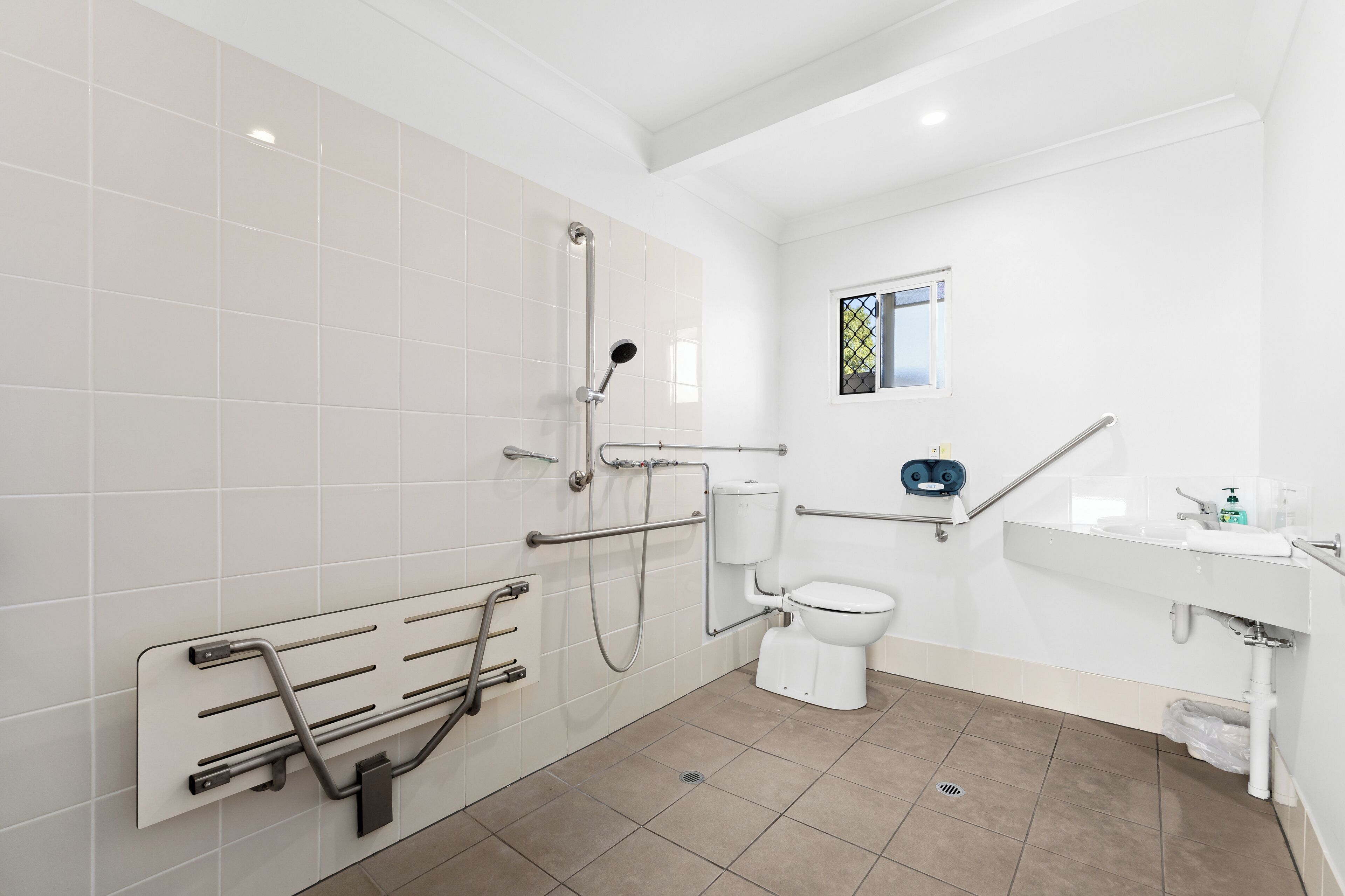 Ein modernes Badezimmer mit Dusche, Toilette und Waschbecken, ausgestattet mit Haltegriffen und einem Fenster.