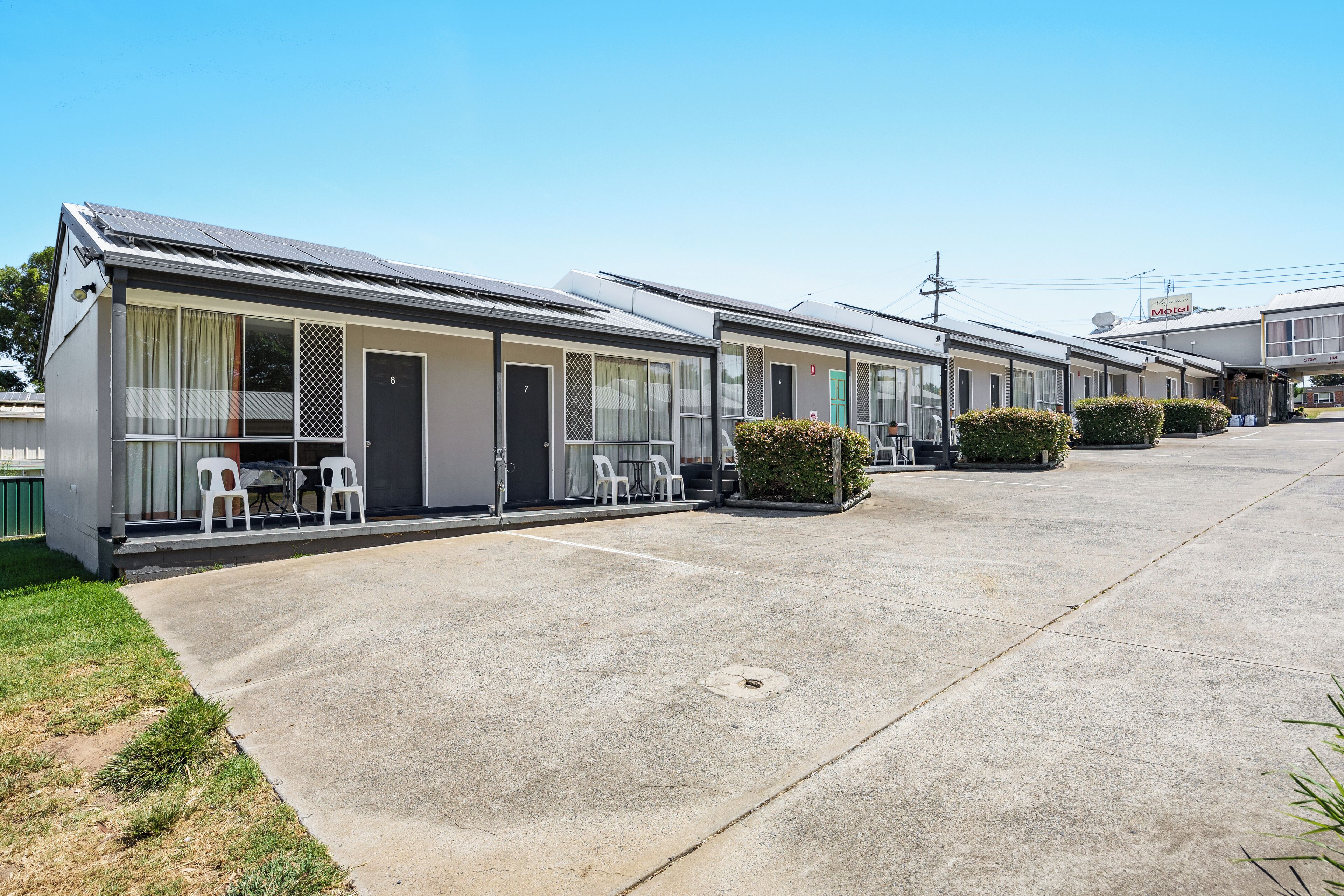 Filas de edificios estilo motel con habitaciones individuales, asientos exteriores y un cielo despejado.