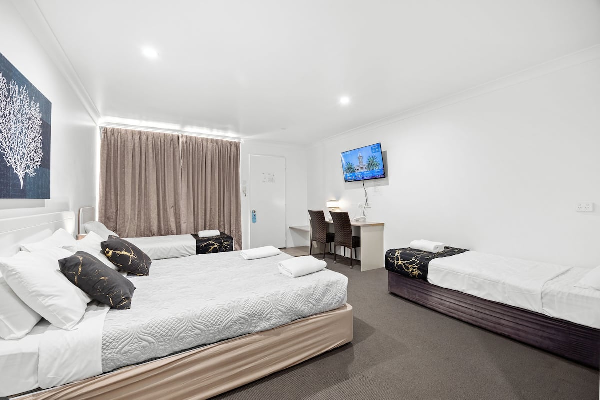 A hotel room with a large bed, a desk, a chair, and a television on the wall.