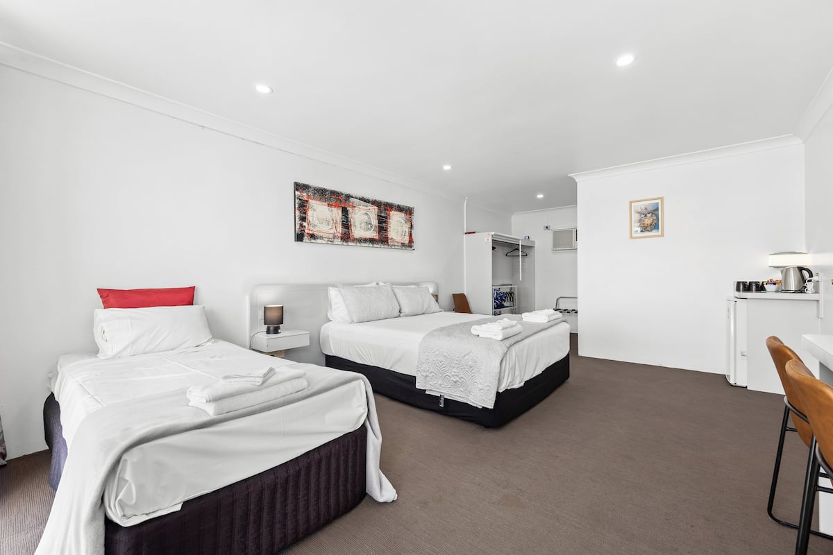 A hotel room with two beds, a desk, a chair, a mirror, and a painting on the wall.