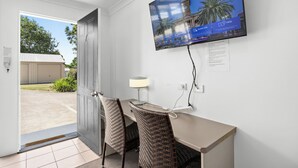 Habitació d'hotel amb televisió que mostra un paisatge urbà, escriptori amb làmpada, cadires de vimet i vista a l'exterior.