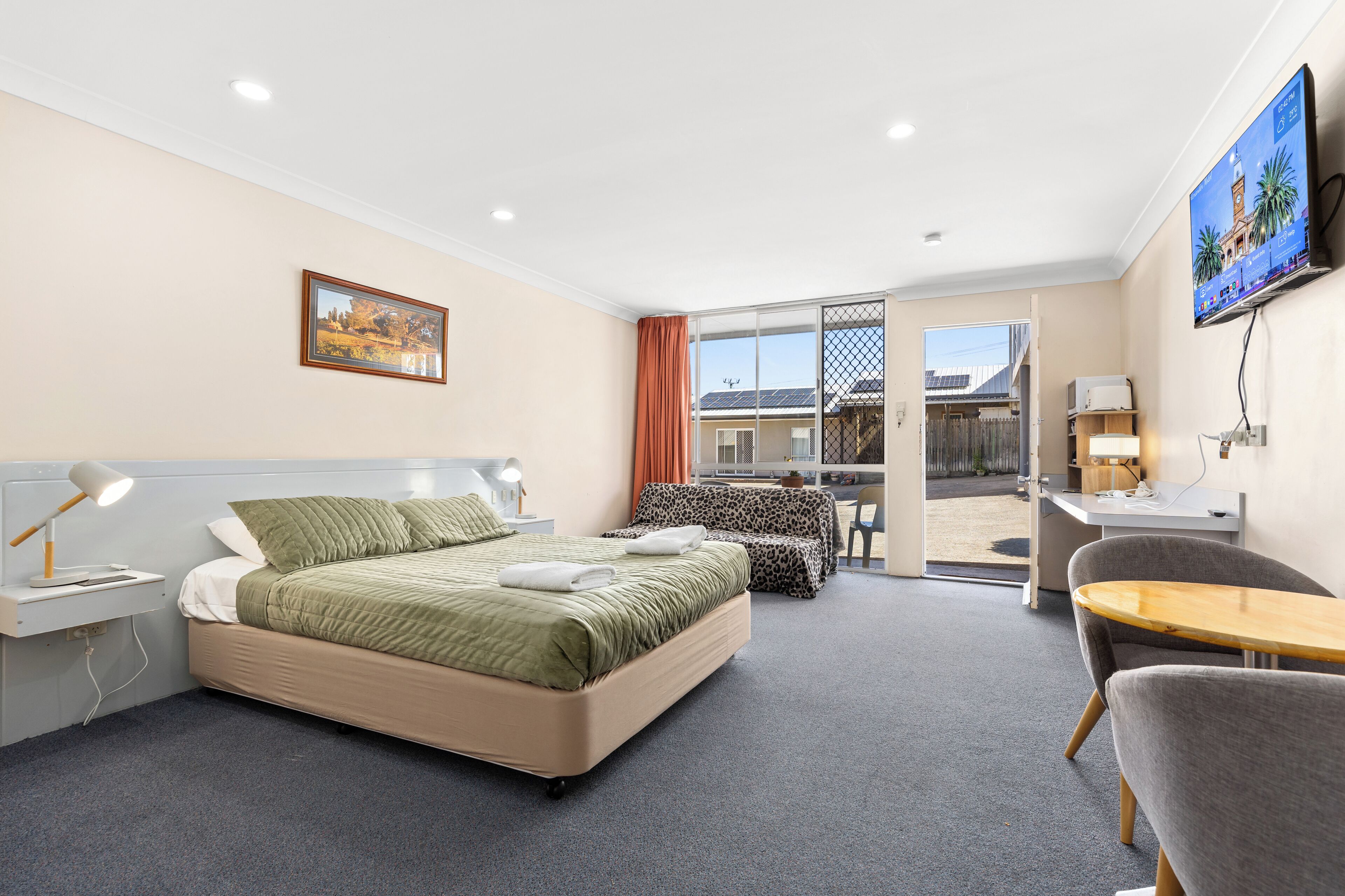 Quarto de hotel com cama, escrivaninha, cadeira, televisão e varanda com vista para um edifício.