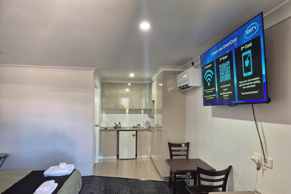 A hotel room with a TV displaying instructions for using SmartCast, a kitchenette, a dining area, and a bed with towels.