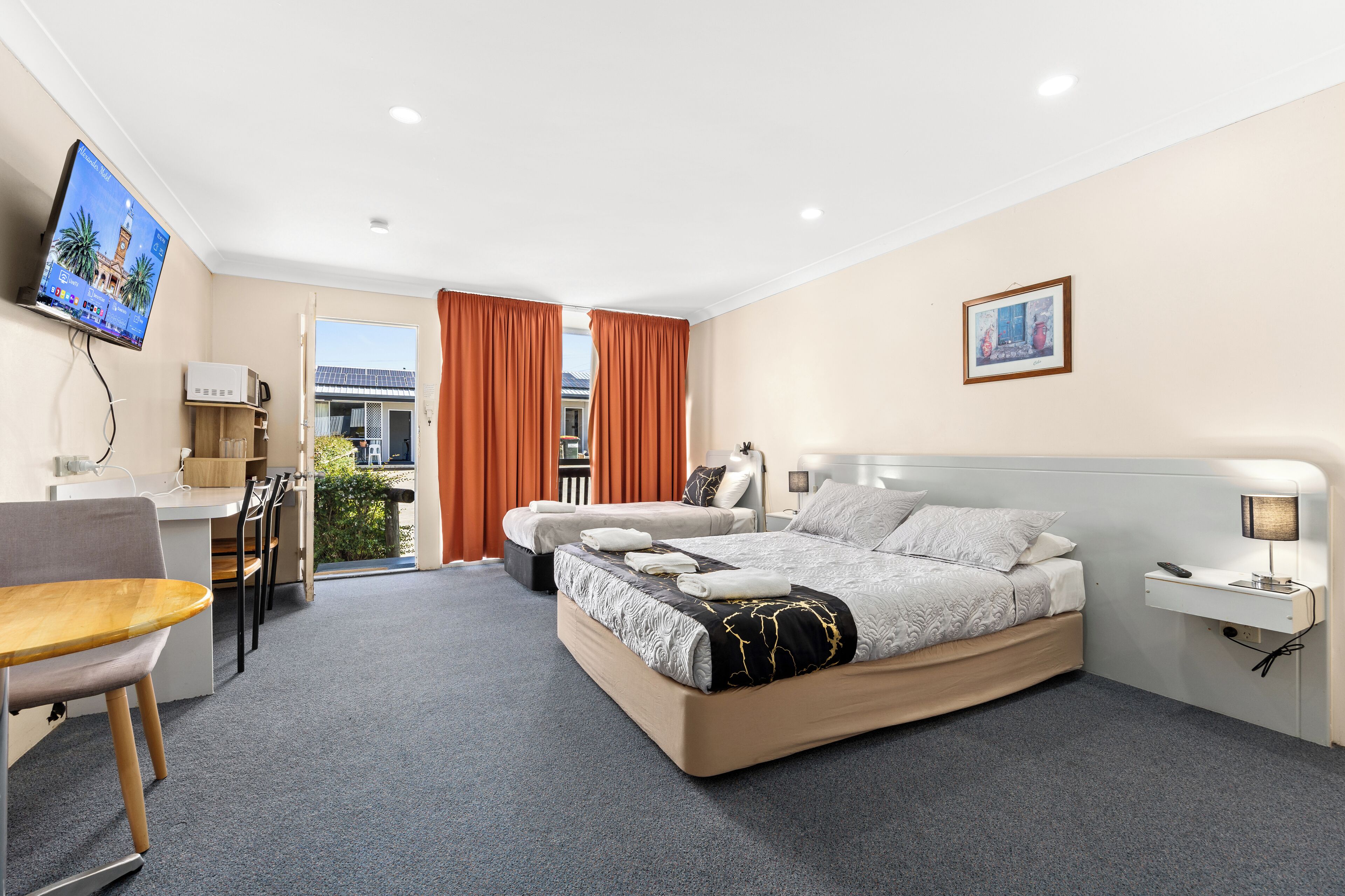 Habitación de hotel con cama, escritorio, silla, televisor y ventana con cortinas.