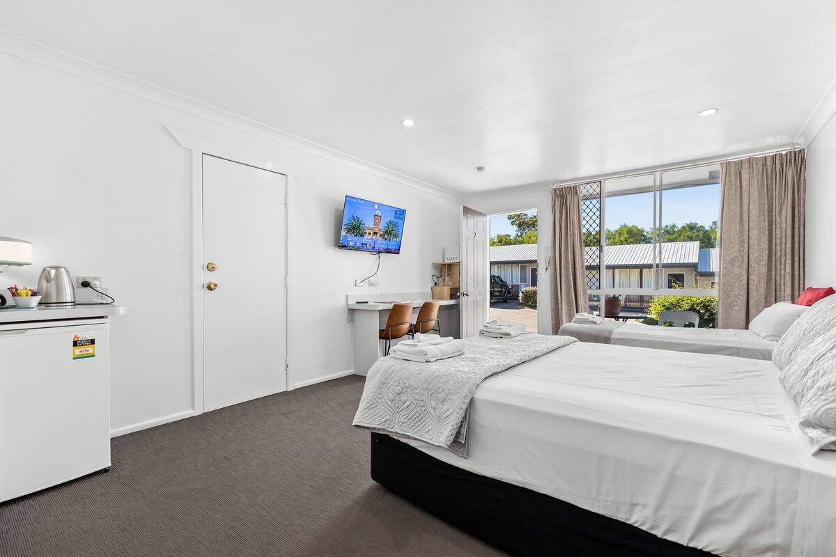 A hotel room with a bed, a desk, a TV, and a view of the outside.