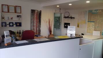 A reception area with a counter, framed certificates, a clock, a map, and a complimentary breakfast sign.