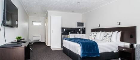 A hotel room with a bed, a desk, a TV, and a kitchenette.