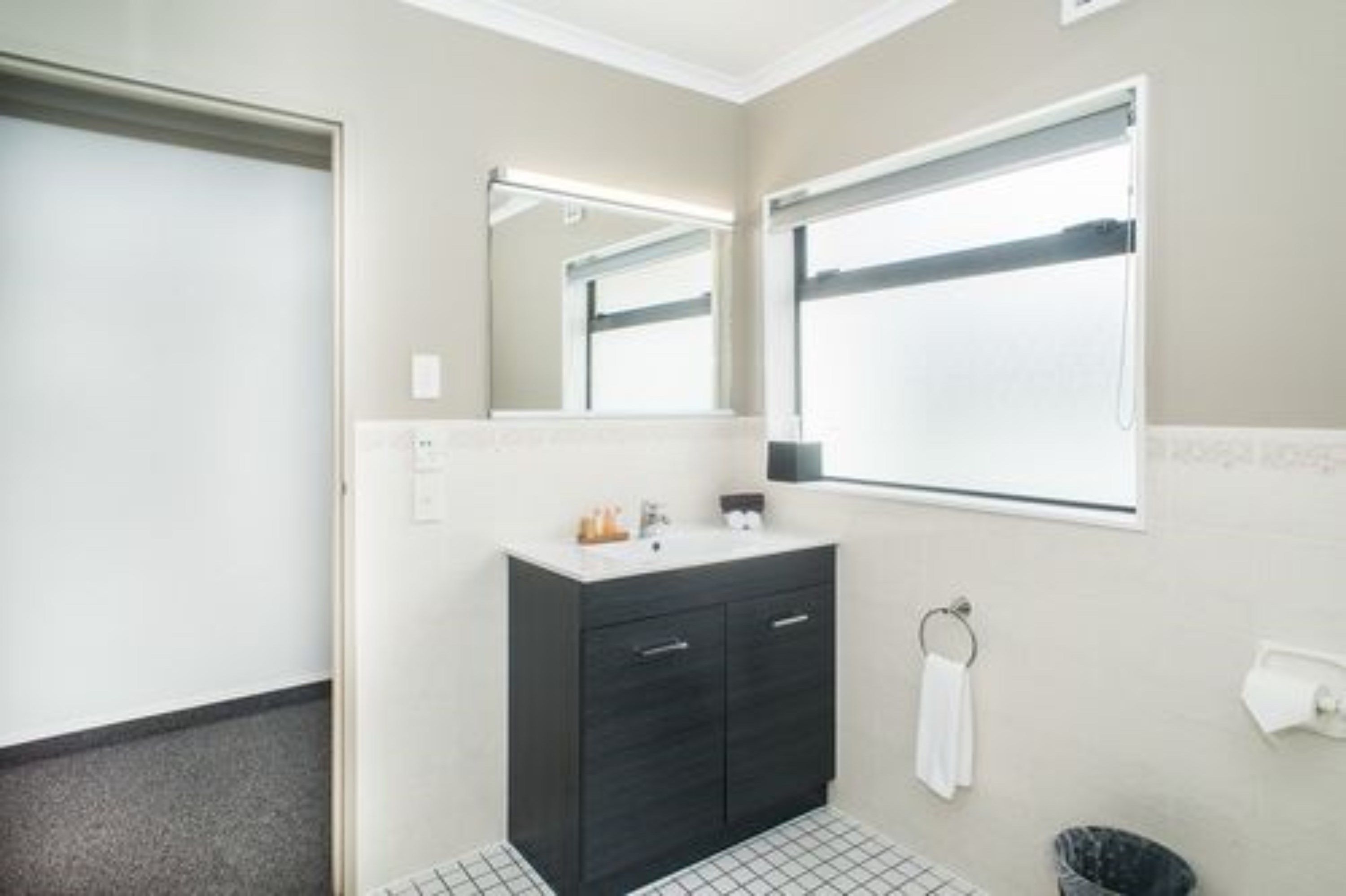Un baño con tocador oscuro, un espejo, un tozalenguas y un dispensador de papel higiénico.