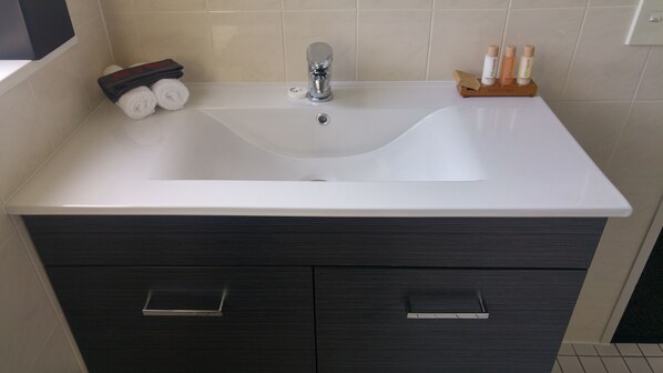 A bathroom with a white sink, dark wood cabinetry, and a small shelf with toiletries. - White Heron Motor Lodge (Gisborne)