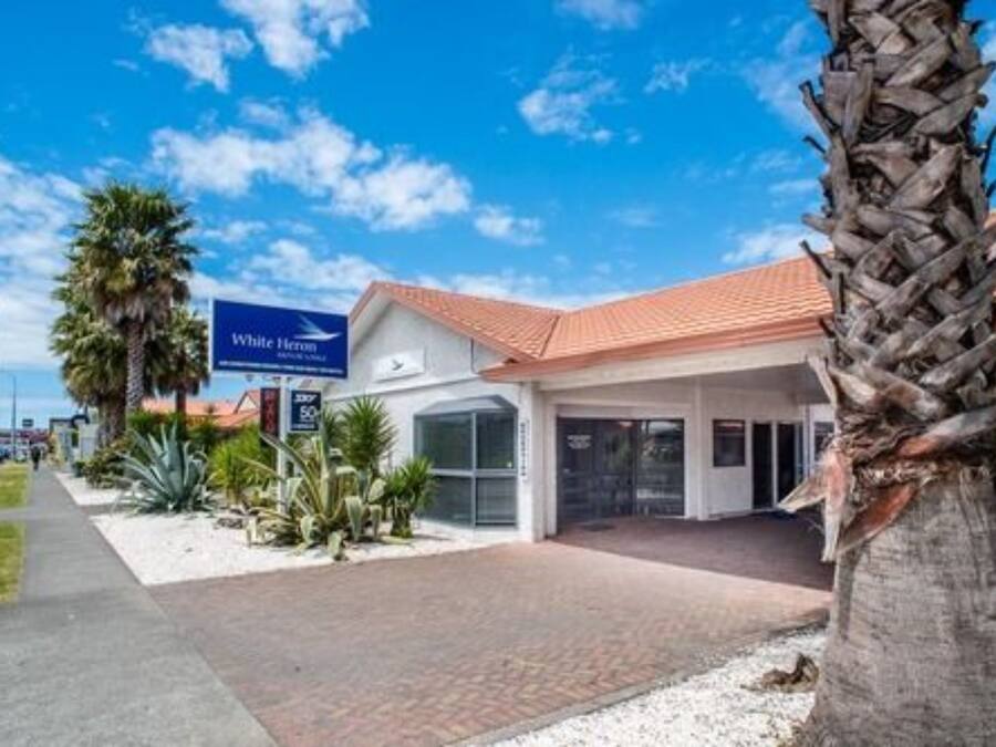 A hotel entrance with a red-tiled roof, palm trees, and a clear blue sky.