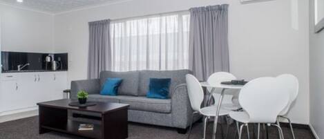 A modern living room with a grey sofa, white chairs, a small table, and a dark coffee table.