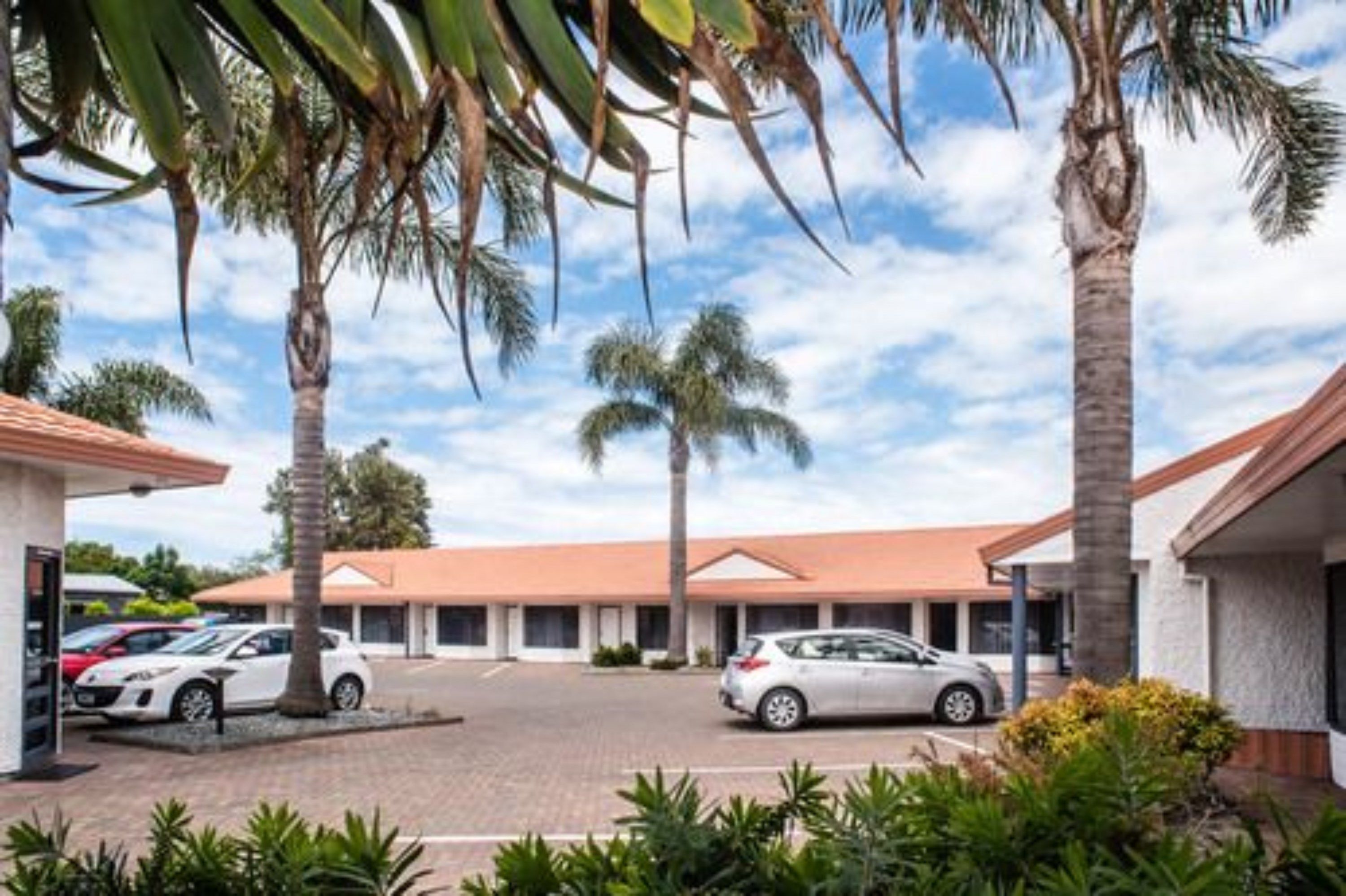 Un hotel con estacionamiento, palmeras y cielo despejado.