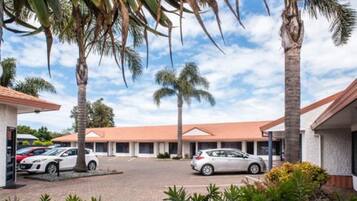 Un hotel con estacionamiento, palmeras y cielo despejado.