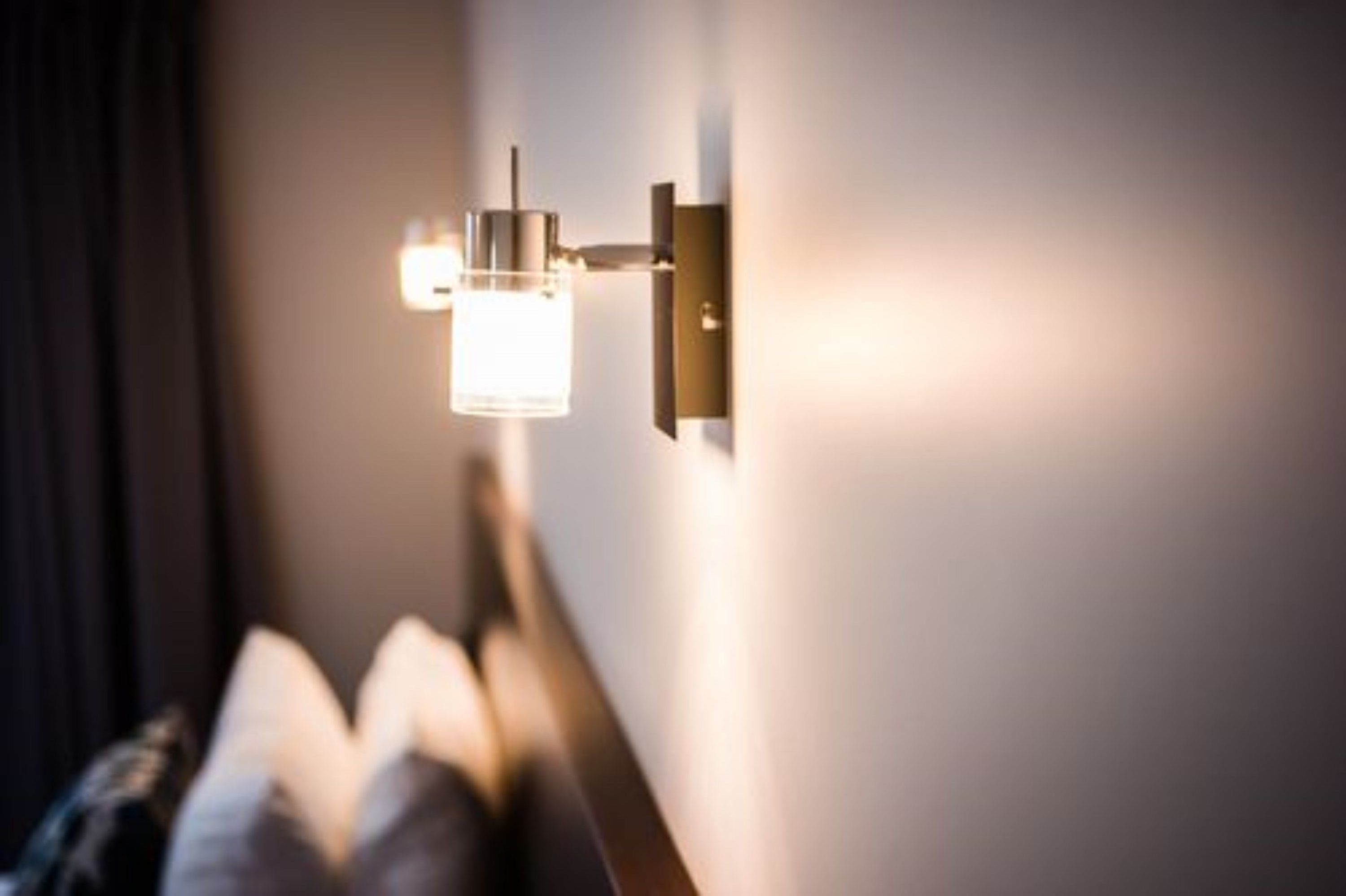 Un luminaire mural au design cylindrique et à la base rectangulaire, diffusant une lumière chaleureuse.