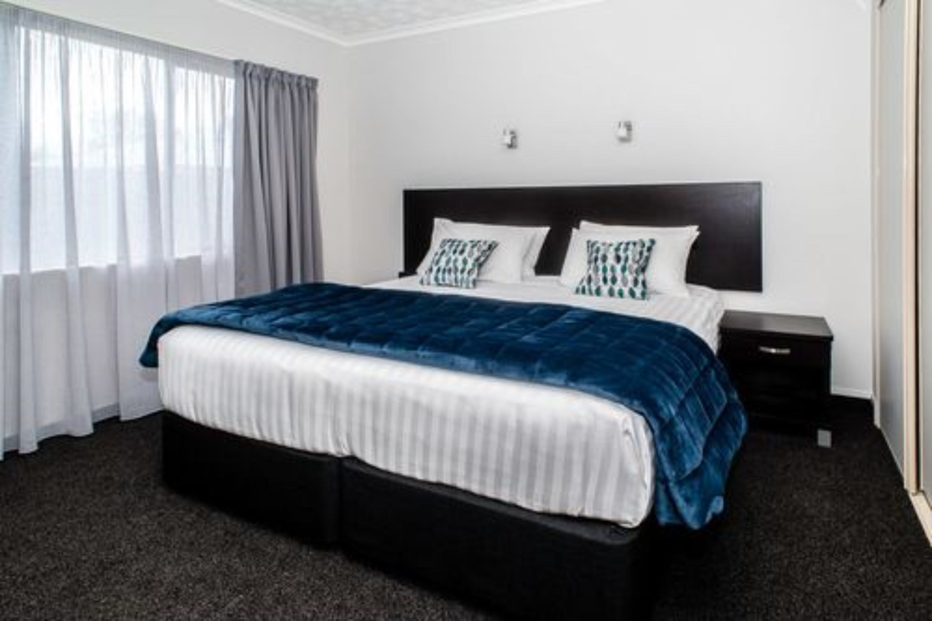 A hotel room with a large bed, a nightstand, and a window with curtains.