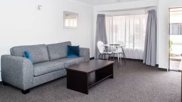 Ein modernes Wohnzimmer mit einem grauen Sofa, einem dunklen Couchtisch und einem weißen Esstisch mit Stühlen.