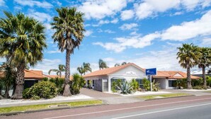 A hotel with a red-tiled roof, palm trees, and a clear blue sky. - White Heron Motor Lodge (Gisborne)