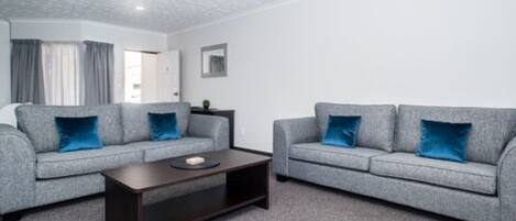 A modern living room with two grey sofas, each with a blue cushion, and a dark wooden coffee table.