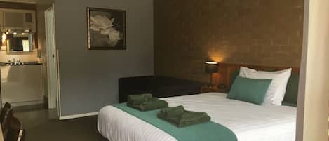 A hotel room with a bed, a nightstand, a lamp, a picture on the wall, and a bathroom visible through an open door.