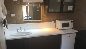Una kitchenette pequeña con un lavamanos blanco, un microondas y un refrigerador.