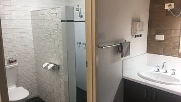 Un baño moderno con pared de ladrillo blanco, cabina de ducha de vidrio, inodoro blanco, lavamanos con espejo y toallero.