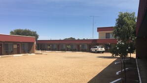 Un motel con un estacionamiento de grava, un coche blanco estacionado al frente y un edificio con techo rojo.