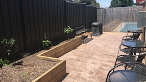 Un espacio al aire libre con un banco de madera, una mesa y una parrilla.