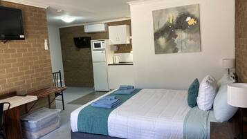 A hotel room with a bed, a desk, a chair, a TV, a microwave, and a kitchenette.