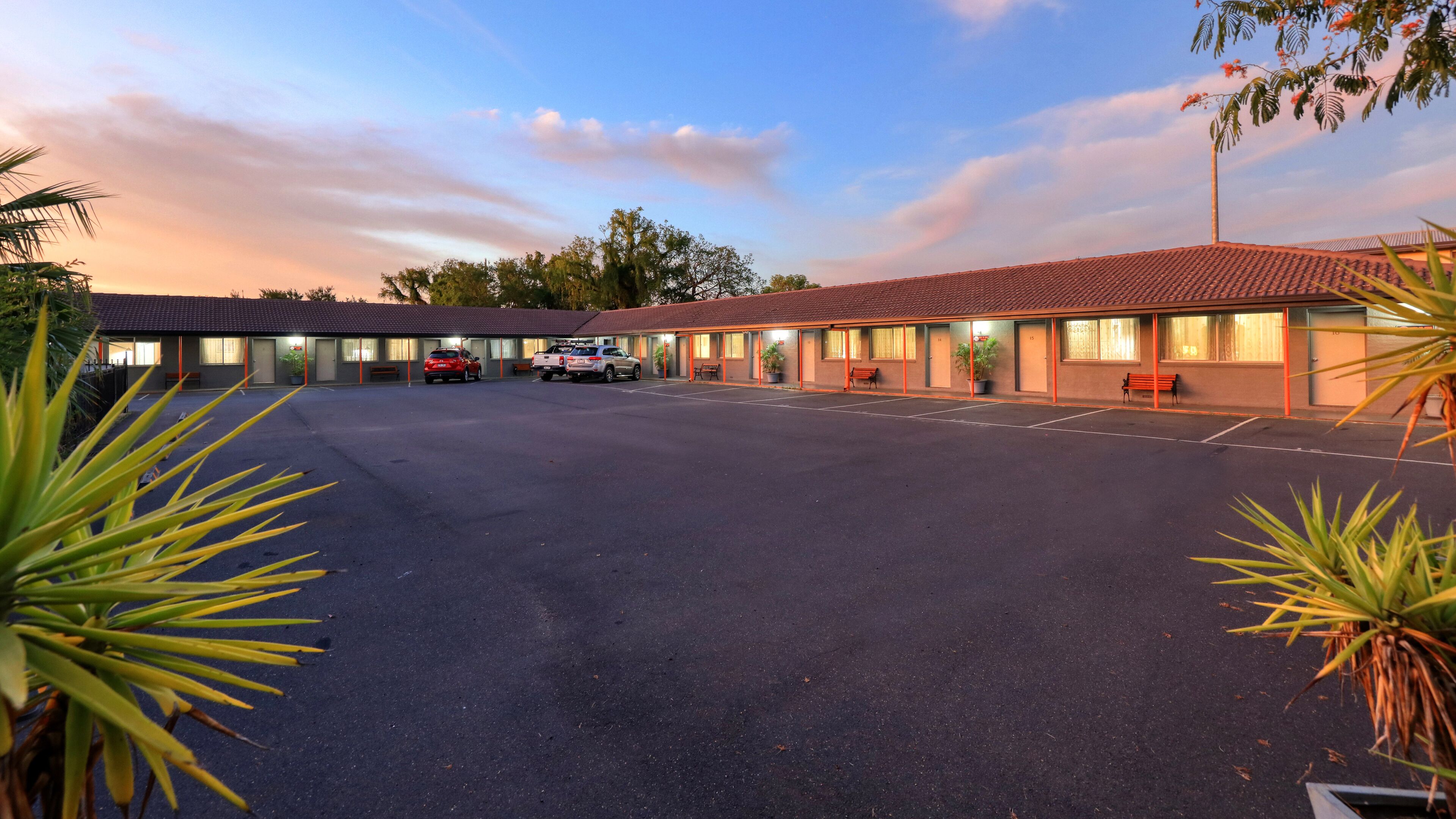 A motel with a large parking lot, multiple rooms, and a few parked cars.