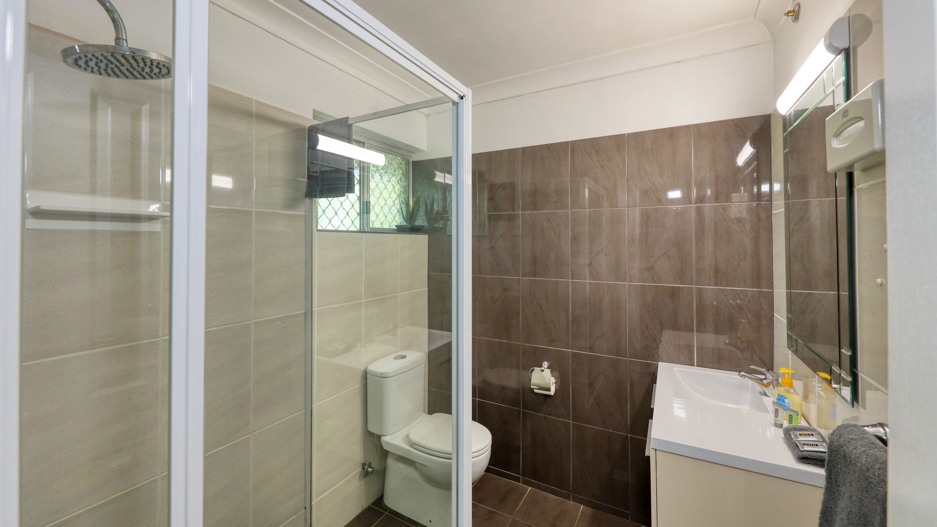 Un baño moderno con ducha de vidrio, inodoro y lavamanos con espejo.