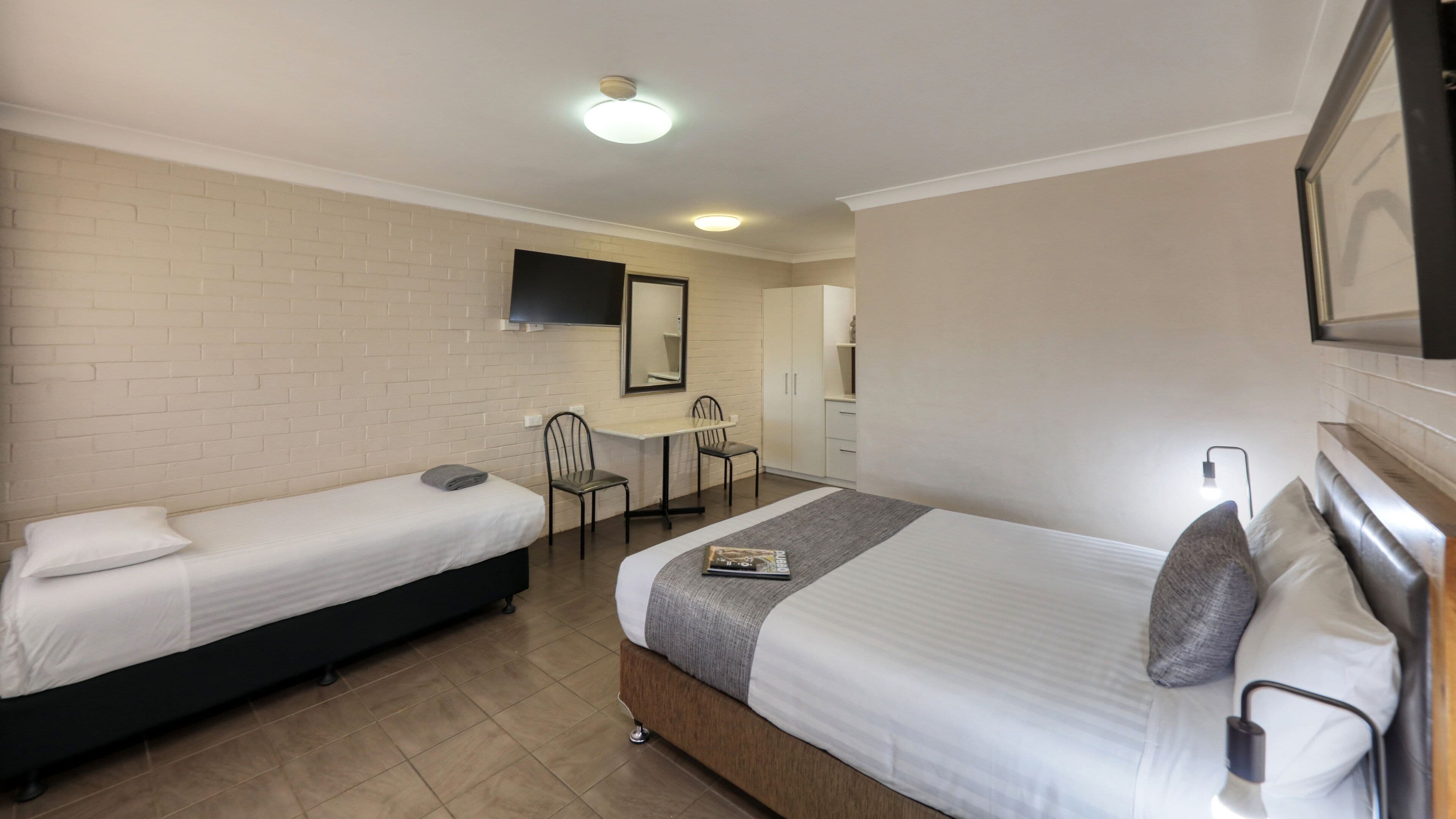 A hotel room with two single beds, a desk with a chair, a TV mounted on the wall, and a mirror above the desk.