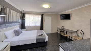 Una habitación de hotel con cama, mesita de noche, lámpara, televisor y un área de comedor con sillas y una mesa.