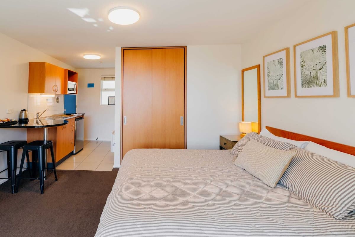 A hotel room with a bed, a desk, and a kitchenette.